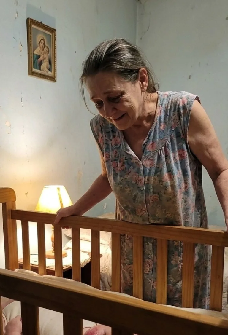 A avó debruçada sobre o berço do neto durante a madrugada, à luz de um abajur